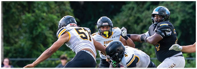 Several people wearing football helmets and uniforms are engaged in a play on a grassy field with trees in the background. Descripci n generada con IA