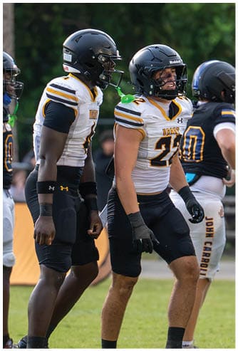 Three people wearing football helmets and uniforms are standing on a field, with one person in a white jersey and two in dark jerseys. Descripci n generada con IA