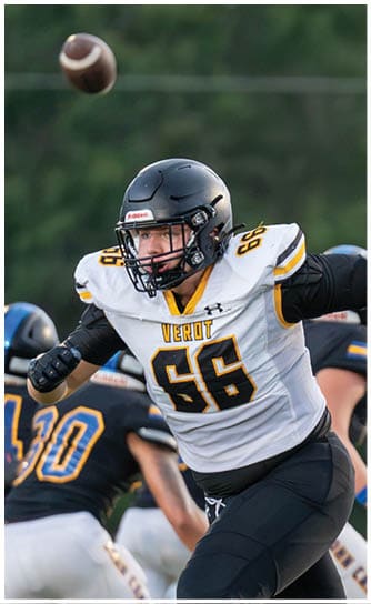 A person wearing a black helmet and a white football jersey with the number 66 and the word “VEROT" is in an athletic stance on a football field with other players in the background. Descripci n generada con IA