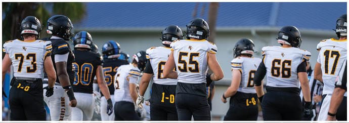A group of people wearing football uniforms with helmets are standing on a field, facing away from the camera. Descripci n generada con IA