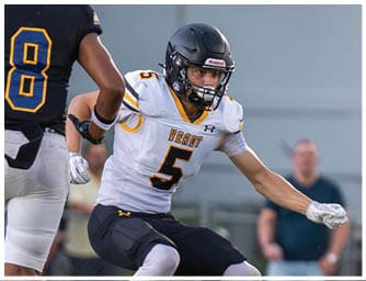 Two people in football uniforms are engaged in a play on the field, with one wearing a black jersey numbered 8 and the other in a white jersey numbered 5. Descripci n generada con IA
