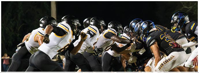 Two opposing American football teams in black and white uniforms are lined up facing each other on a field under stadium lights. Descripci n generada con IA