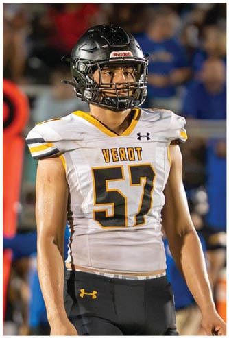 A person wearing a white football jersey with the number 57 and the word “VEROT" stands on a field with a black helmet and a focused expression. Descripci n generada con IA