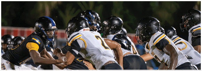 Several people wearing football helmets and uniforms are engaged in a game or practice on a field at night. Descripci n generada con IA