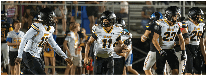 Four people in football uniforms with helmets are on a field, with one person holding a football and others appearing ready to move. Descripci n generada con IA