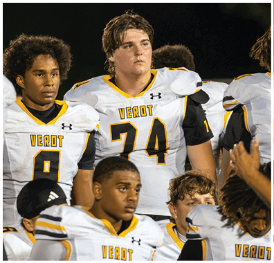 A group of people wearing white and yellow football uniforms with the word “VEROT" on the front are standing closely together, appearing attentive or focused. Descripci n generada con IA