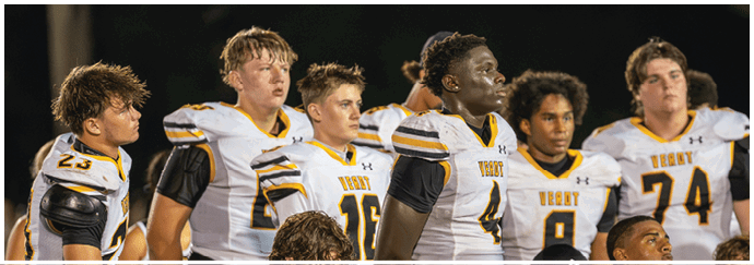 A group of people wearing white and yellow football uniforms stand closely together on a field at night. Descripci n generada con IA