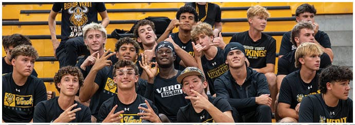 A group of people wearing matching black t-shirts with a tiger logo are sitting and standing on bleachers in a gymnasium. Descripci n generada con IA