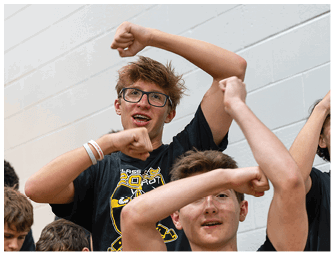 A person with glasses and braces is raising their arms and smiling enthusiastically indoors. Descripci n generada con IA