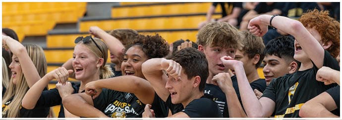 A group of people wearing matching sports shirts are enthusiastically flexing their arms and smiling in a gymnasium setting. Descripci n generada con IA