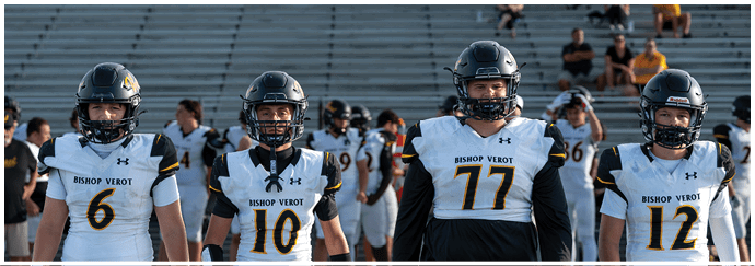 Four people wearing football helmets and white Bishop Verot jerseys stand side by side on a field with empty bleachers in the background. Descripci n generada con IA