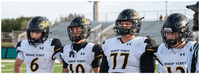 Four people wearing football helmets and white jerseys with “Bishop Verot" written on them stand side by side on a sports field with empty bleachers in the background. Descripci n generada con IA
