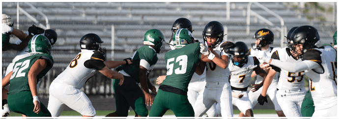 People wearing green and white football uniforms are actively engaged in a play on a football field. Descripci n generada con IA