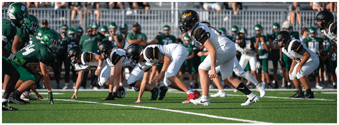 Two opposing American football teams in green and white uniforms are lined up on a field preparing for the next play. Descripci n generada con IA