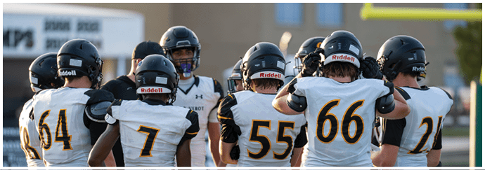 A group of people wearing football helmets and white jerseys with black and gold numbers are gathered closely on a field. Descripci n generada con IA