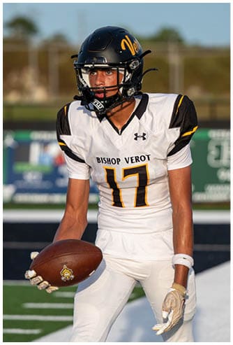 A person wearing a black football helmet and a white Bishop Verot football uniform with the number 17 is holding a football and appears focused on the game. Descripci n generada con IA