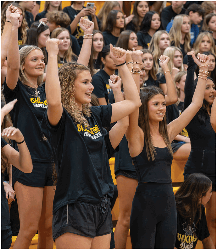 A group of people wearing black athletic clothing are standing closely together with their arms raised and fists clenched, appearing to cheer or celebrate indoors. Descripci n generada con IA