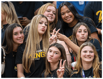 A group of smiling and playful people wearing matching black shirts with yellow text pose closely together, some making peace signs. Descripci n generada con IA