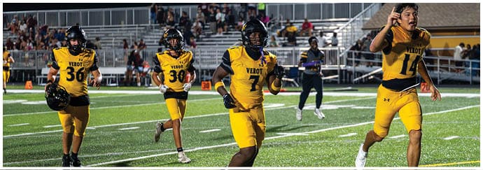 Four people in yellow football uniforms are running on a field with a crowd in the background. Descripci n generada con IA