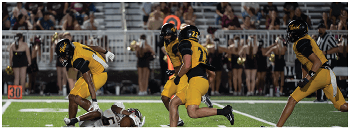 A group of people in yellow and black sports uniforms are playing football on a field with one person on the ground and others running or preparing to move. Descripci n generada con IA