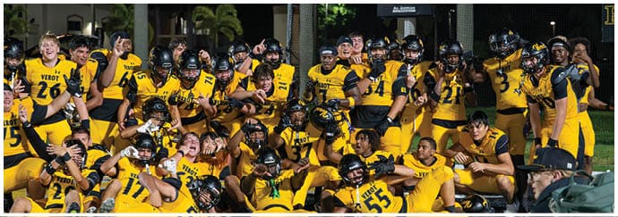 A large group of people wearing yellow and black football uniforms are gathered closely together outdoors at night, posing and celebrating. Descripci n generada con IA