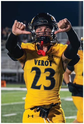 A person wearing a yellow and black football uniform with the number 2 is on a football field at night, raising their hand with a thumbs-up gesture. Descripci n generada con IA