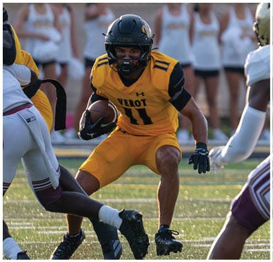 A person in a yellow football uniform is running with the ball while two people in white uniforms prepare to block or tackle on a football field. Descripci n generada con IA