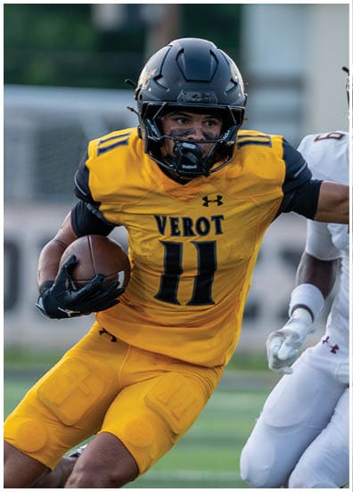 A person in a yellow football uniform with the number 11 is running with the ball while being pursued by another person in a white football uniform with the number 9 on a football field. Descripci n generada con IA