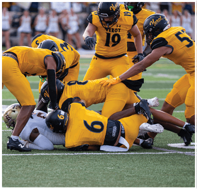 Several football players in yellow uniforms are tackling a player in a white uniform on a field during a game. Descripci n generada con IA
