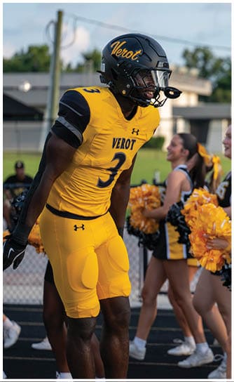 A person wearing a yellow and black football uniform with the number 3 stands near cheerleaders holding yellow and black pom-poms. Descripci n generada con IA