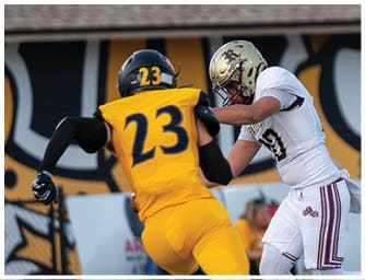 Two people in football uniforms are engaged in a play on the field, with one wearing a black jersey numbered 8 and the other in a white jersey numbered 5. Descripci n generada con IA