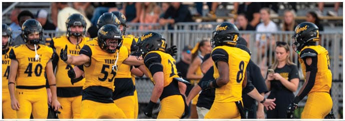 A group of people wearing yellow and black football uniforms are gathered on a field with a few people in casual clothing standing nearby. Descripci n generada con IA