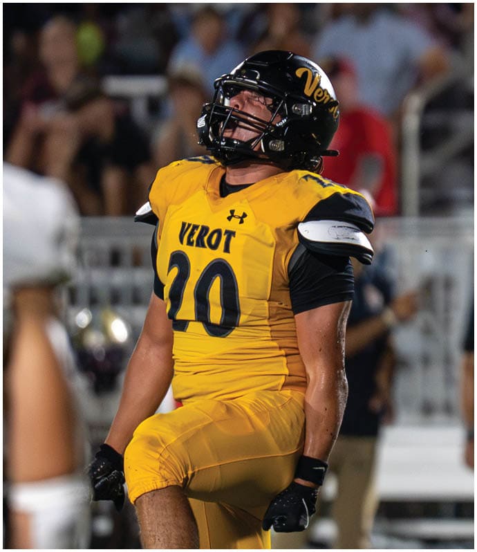 A person in a yellow football uniform with the number 20 is on the right side of the image facing a person in a white football uniform with the number 8 and a gold helmet, with a blurred crowd in the background. Descripci n generada con IA