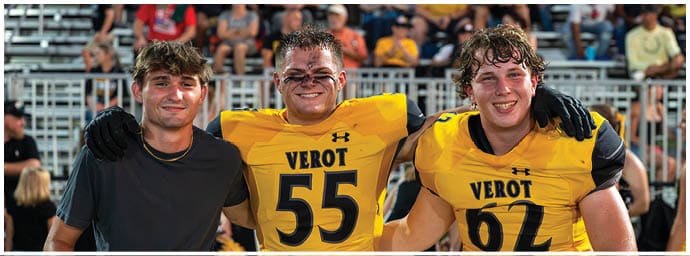 Three people with wet hair are smiling and posing together on a sports field, with two wearing yellow football jerseys labeled “VEROT" and one in a black shirt. Descripci n generada con IA