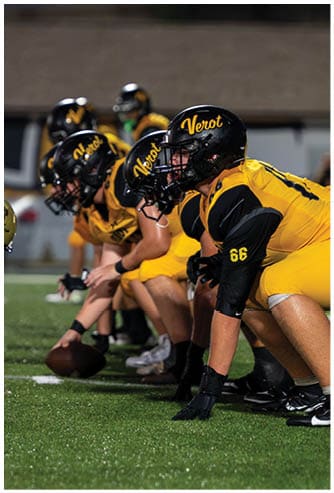 A person wearing a yellow and black sports uniform is bending forward, with a blurred background suggesting an indoor sports setting. Descripci n generada con IA