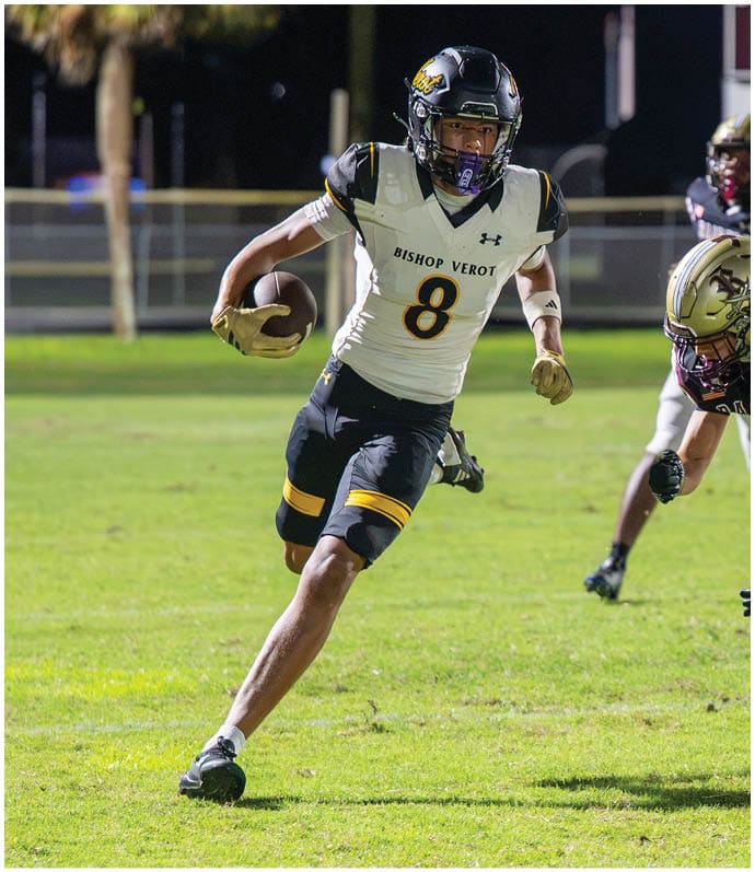 An adult wearing a white and black football uniform with the number 8 is running with the ball while two adults in black and gold football uniforms attempt to tackle on a grassy field at night. Descripci n generada con IA