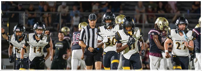 Two people wearing black helmets and sports gear are engaged in an outdoor activity with a blurred banner in the background. Descripci n generada con IA