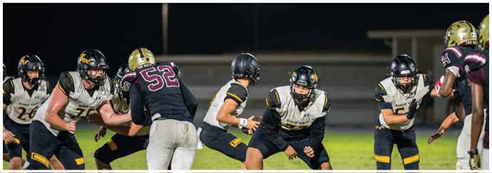 A group of people wearing football helmets and white jerseys with black and gold numbers are gathered closely on a field. Descripci n generada con IA