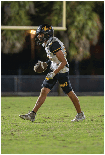 A person wearing a black football helmet and a white Bishop Verot football uniform with the number 17 is holding a football and appears focused on the game. Descripci n generada con IA