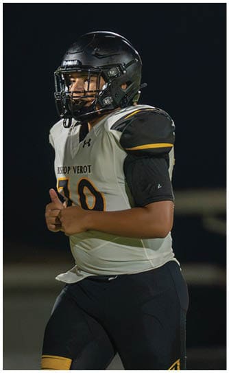 A person wearing a football uniform is kicking a ball on a grassy field with one leg raised high and the other planted on the ground. Descripci n generada con IA