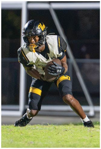 Two people in football uniforms are engaged in a play on a field, with one holding the ball and the other preparing to receive or block. Descripci n generada con IA