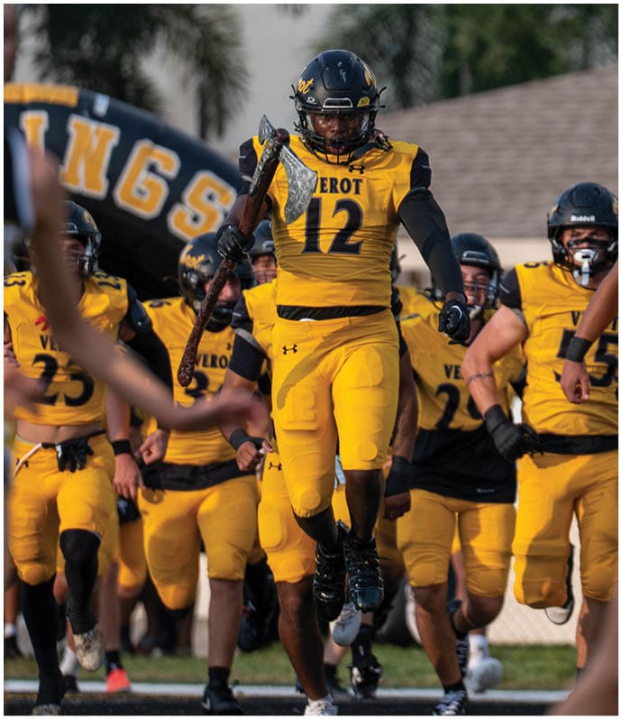 A group of people in yellow and black football uniforms are walking forward with one person in front holding a large axe. Descripci n generada con IA