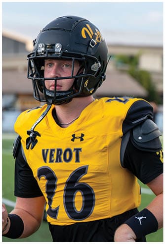 A person wearing a yellow and black football uniform with the word “VEROT" and the number 26 on the jersey is standing on a field while wearing a black helmet. Descripci n generada con IA