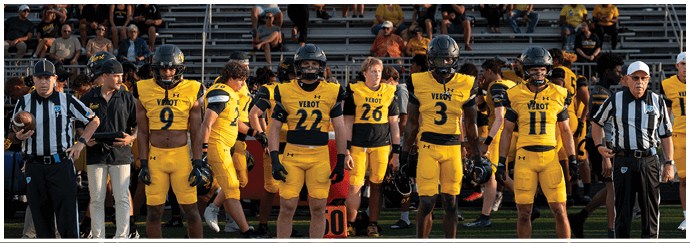 A group of people in yellow and black football uniforms and referees in striped shirts stand on a football field with bleachers and spectators in the background. Descripci n generada con IA