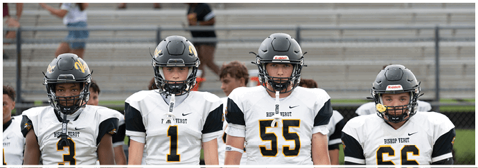 Four people wearing football helmets and white Bishop Verot jerseys stand side by side on a field with empty bleachers in the background. Descripci n generada con IA