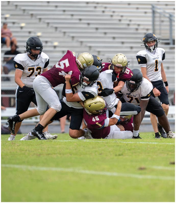 Several people wearing football uniforms and helmets are gathered on a field with one person in green facing away and others in white standing or crouching nearby. Descripci n generada con IA