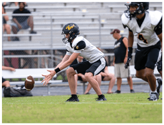 An adult wearing a backward cap adjusts the helmet of a person in a football uniform with the number seven on it during a practice or game. Descripci n generada con IA