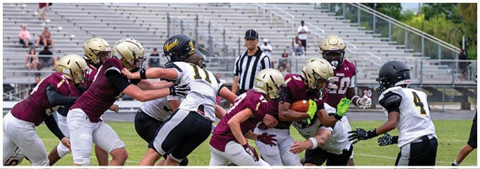 People wearing green and white football uniforms are actively engaged in a play on a football field. Descripci n generada con IA