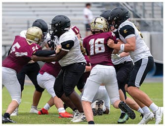 Three people in football uniforms with helmets are actively engaged in a game on a field with others in the background. Descripci n generada con IA
