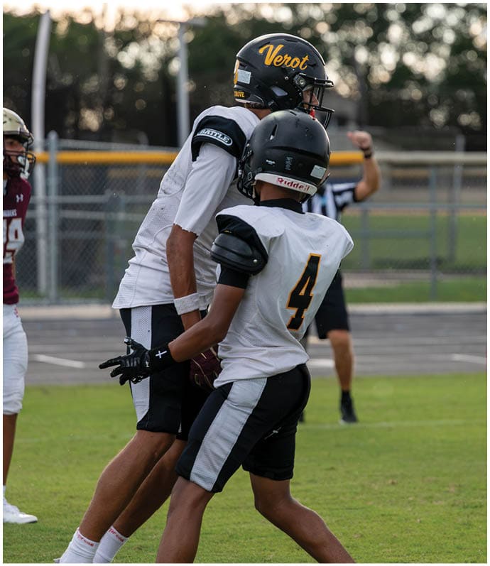 Two people in football uniforms are actively playing on a field at night, with one kicking the ball and the other preparing to block. Descripci n generada con IA